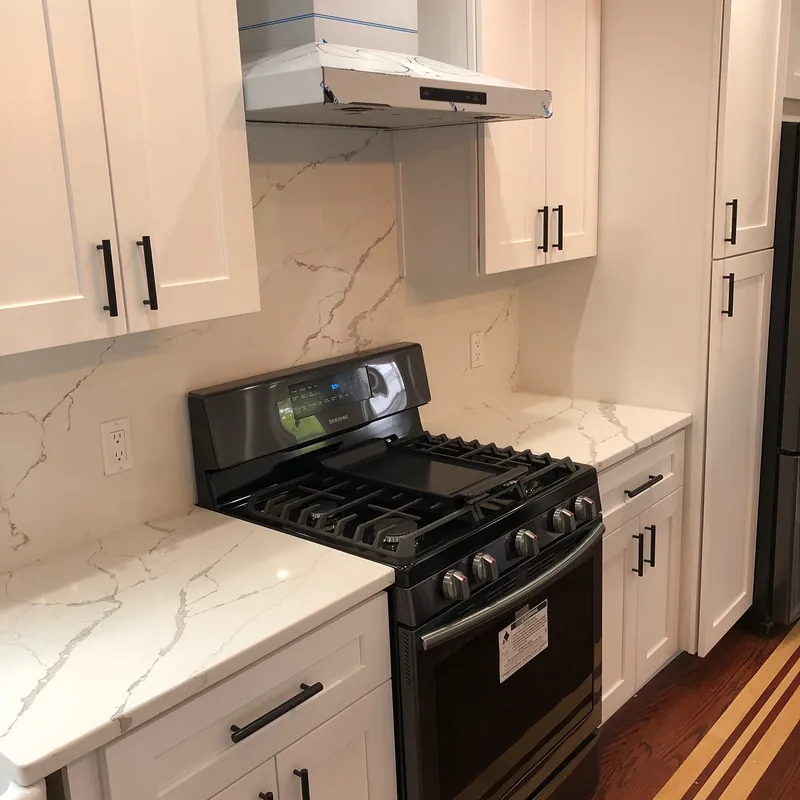 Calacatta quartz counters with a matching full-height splash around a black range, Osterville, MA