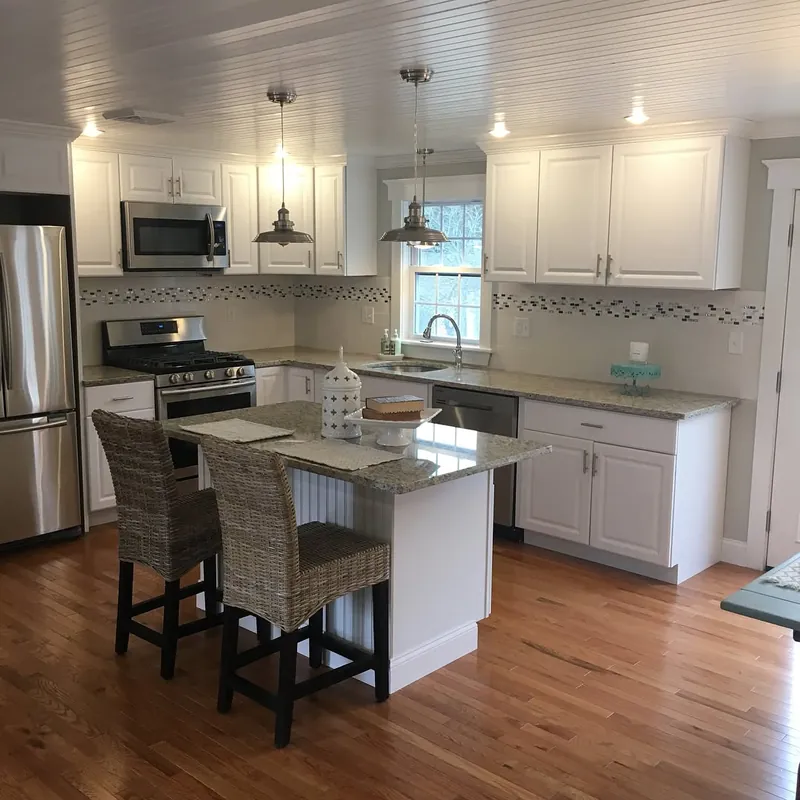 White kitchen with a speckled granite island, wicker stools and pendant lights, South Yarmouth, MA