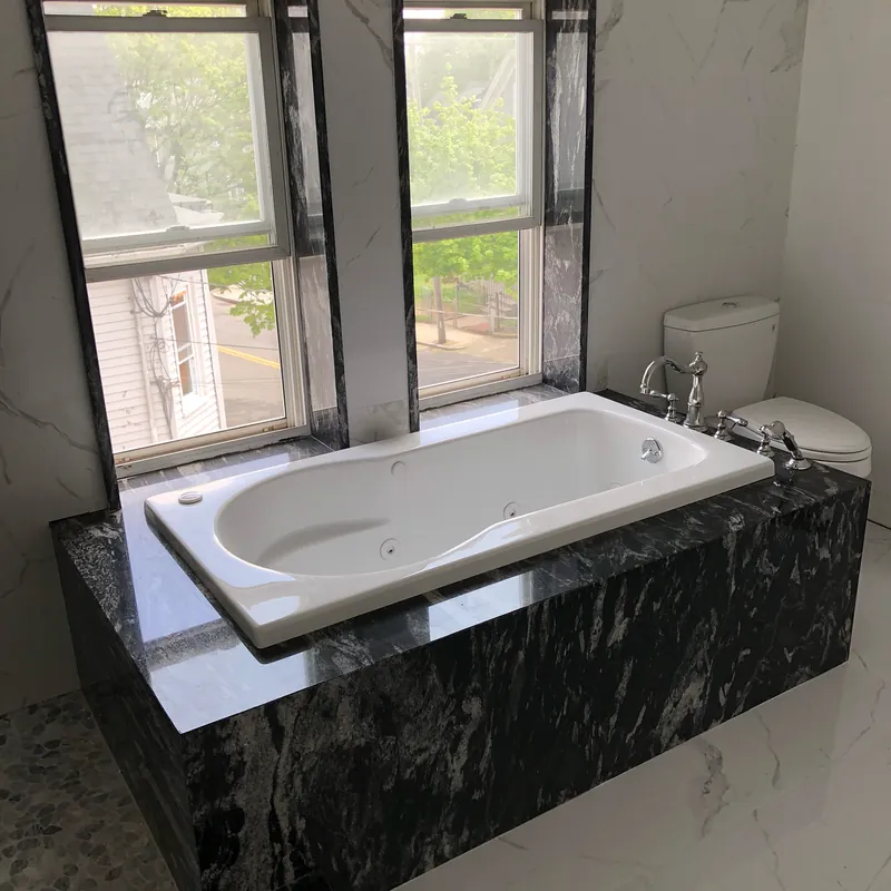 Tub deck and surround in black granite with white veining and a mitered edge, set between two windows, Malden, MA