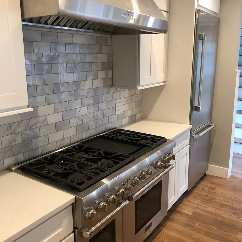 White quartz counters beside a professional range with a gray tile backsplash, Osterville, MA