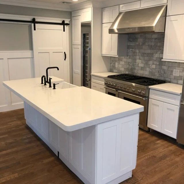 Long white quartz island with black faucet and professional range