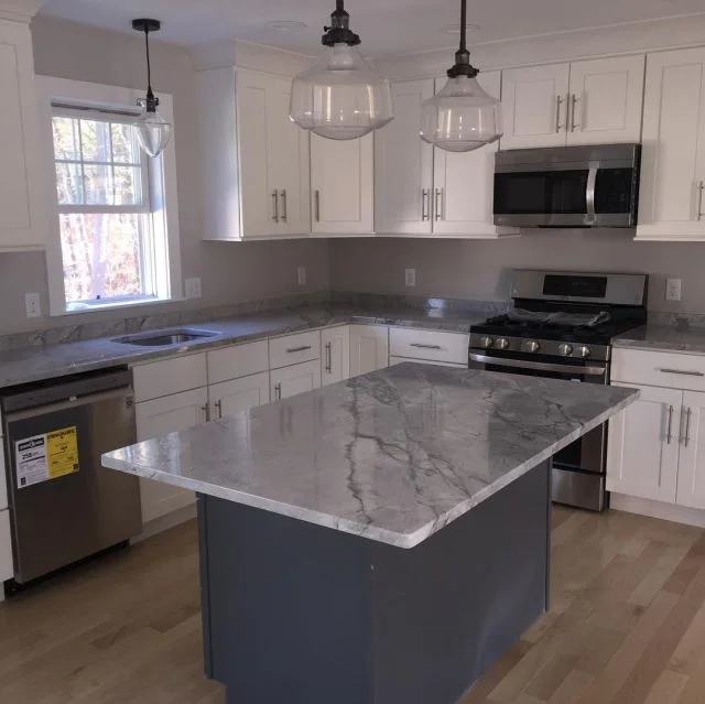 White kitchen with light grey quartzite island and glass pendants