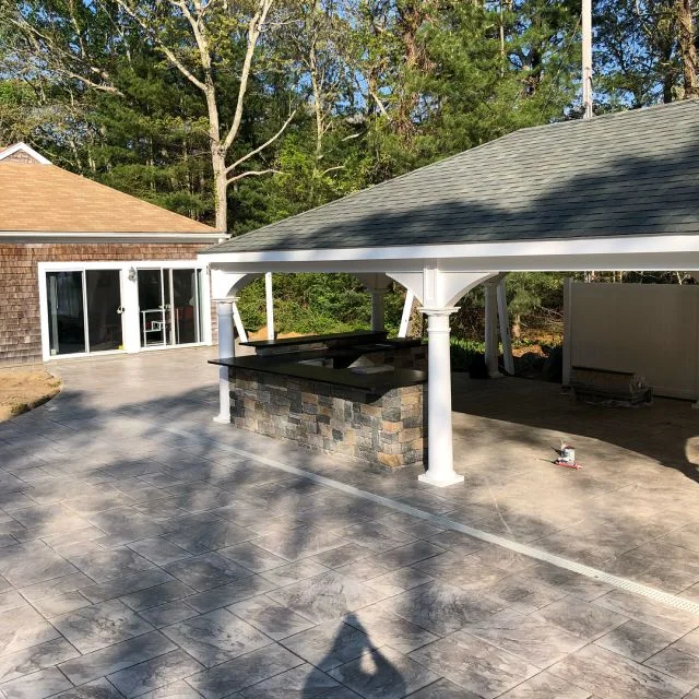 Outdoor kitchen under a pergola with a black granite counter on a natural stone base, Cape Cod patio